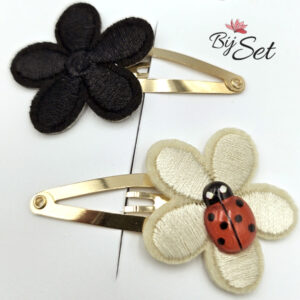 crème en zwarte bloem op haarspeldje met een lieveheersbeestje